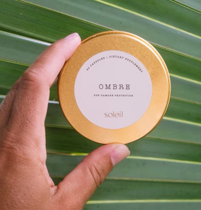 Ombré sun protection supplement held against green palm leaves